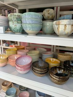 bowls and plates are on shelves in a store, some have been painted with different colors