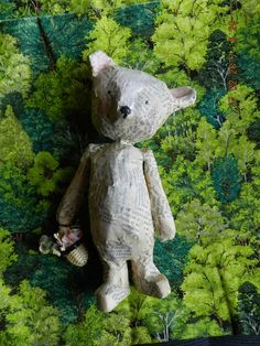 a teddy bear made out of newspaper sitting in the middle of a forest with trees