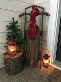 a wooden sled with two lanterns and a scarf on it sitting next to a christmas tree