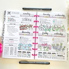 an open planner book sitting on top of a desk next to a pen and flowers