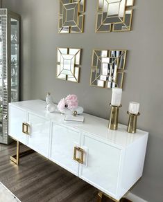 a white dresser with gold accents and mirrors on the wall above it, along with candles