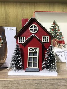 a small red house with trees on the shelf next to it and a glass vase