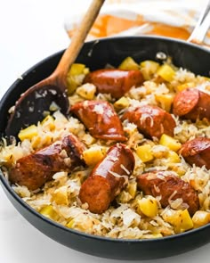 sausage and pineapple rice in a skillet with wooden utensils on the side