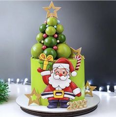 a green christmas cake with santa clause on top and decorations around the base, sitting on a white plate