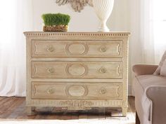 a white dresser sitting in a living room next to a chair and table with a plant on top