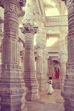 two women in white dresses are walking through an ornately decorated building with columns and pillars