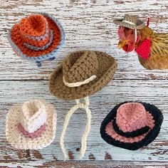 four crocheted hats are sitting on a white wooden surface and one is wearing a rooster hat