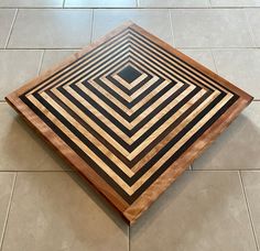 a square shaped wooden table with black and white squares on the top, sitting on a tile floor