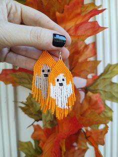 a person holding up a pair of beaded earrings with two dogs on them and orange leaves in the background