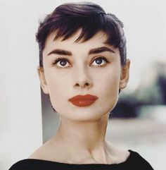 a woman with short hair and red lipstick looks at the camera while wearing a black dress