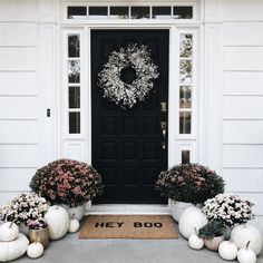 two white pumpkins sitting in front of a black door with a wreath on it