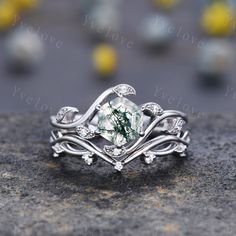 a close up view of a ring with green and white stone in the center, on top of a rock