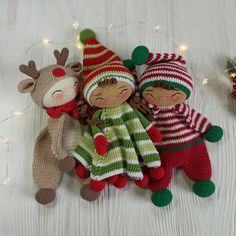 three knitted christmas dolls laying next to each other on a white surface with lights in the background