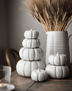 white ceramic pumpkins are stacked on top of each other in front of a vase