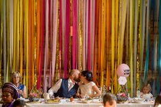 a bride and groom sitting at a table in front of colorful streamers