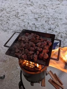 a grill that has some meat on it and flames in the snow next to it