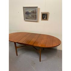 an oval wooden table with two pictures on the wall