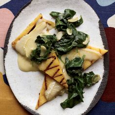 a white plate topped with slices of pizza covered in cheese and spinach on top of a colorful table cloth