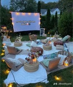 an outdoor movie is set up in the grass with many pillows and lights around it