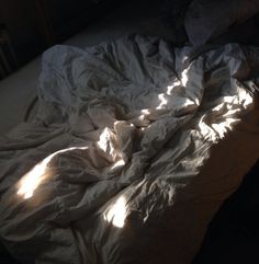 an unmade bed with white sheets and sunlight coming through the window on top of it