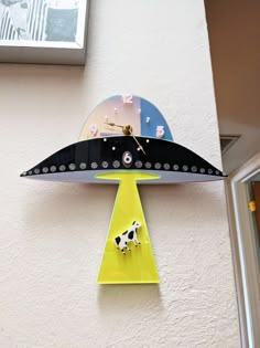 a clock with a cow on it hanging from the side of a wall next to a window