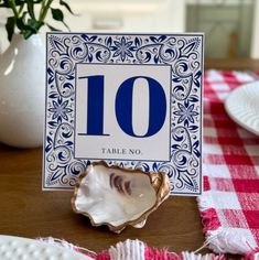 a table number with a shell on it and a red checkered table cloth in the background