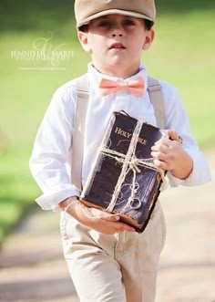 a young boy wearing a hat and suspenders holding a book with a bow tie