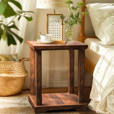 a small wooden table sitting on top of a bed next to a lamp and pillows