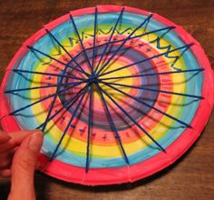 a hand holding a colorful paper plate with sticks sticking out of the center and writing on it