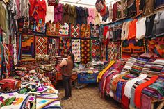 a woman standing in front of a store filled with lots of colorful fabrics and rugs