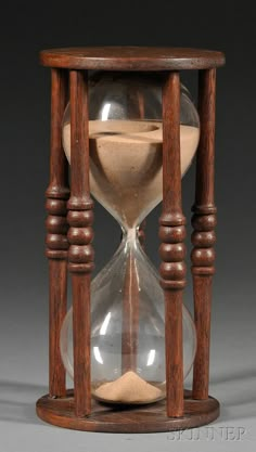 an old wooden hourglass with sand running through the bottom and inside, on a gray background