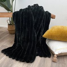 a black blanket sitting on top of a wooden floor next to pillows and a plant