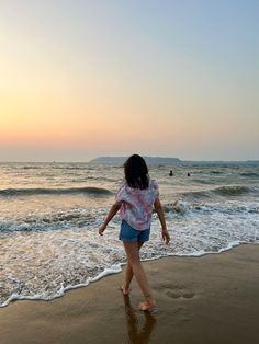 a woman walking along the beach at sunset