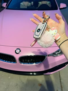 a person holding a cell phone in front of a pink car with hello kitty keychain on it