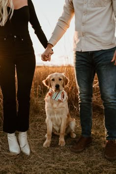 a man and woman holding hands while standing next to a brown dog in a field