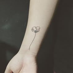 a small flower tattoo on the wrist is shown in black and white ink, with an outline of a single flower