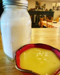 a red bowl filled with yellow liquid next to a mason jar on a wooden table