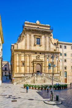 an old building with a fountain in front of it and people walking around the courtyard