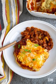 a white plate topped with an omelet covered in beans and cheese next to a casserole dish