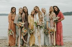 a group of women standing next to each other on a beach holding bouquets and flowers