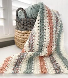 there is a crocheted blanket on the table next to a basket with yarn