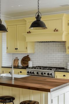 a kitchen with yellow cabinets and black pendant lights over the stove top, along with two stools