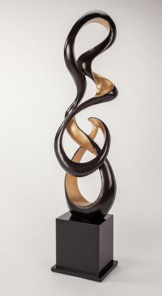 an abstract sculpture is shown on a black stand with gold accents and a white background