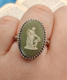 a person's hand holding a ring with a statue on it