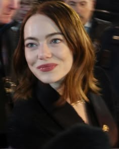 a close up of a person wearing a suit and smiling at the camera with other people in the background