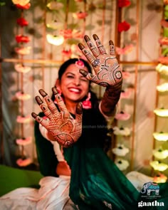 a woman sitting down with her hands painted in hendi and flowers on the wall behind her