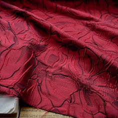 an old book is laying on the floor next to a red flowered cloth that has been draped over it