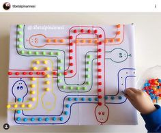 a child's hand is pointing at a game on a board with lights and beads