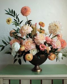 a vase filled with lots of flowers on top of a green table next to a white wall