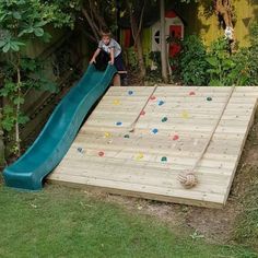 a young boy sliding down a slide in the back yard on a wooden decked area